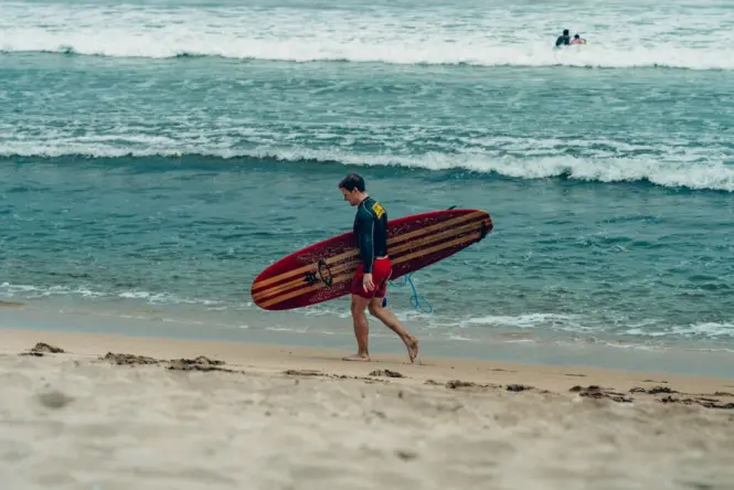 A beginner surfer catches a gentle whitewater wave on a soft-top longboard at Kuta Beach