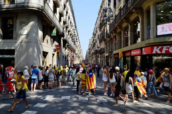 A busy tourist crowd walking along a tree-lined street in Barcelona