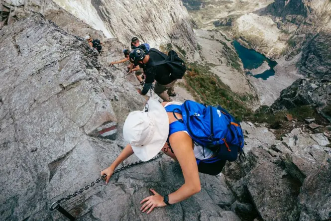 Hikers gripping fixed chains on the exposed rock section of Lion's Head