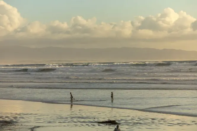 Children wading in shallow water at Muizenberg Beach with lifeguard tower nearby