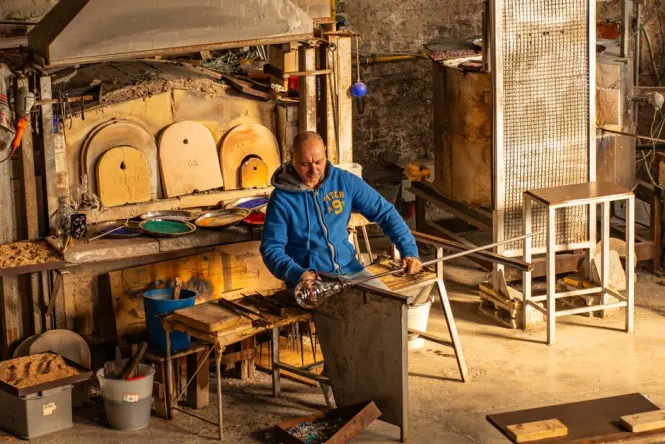 A master glassblower shaping molten glass in a hot furnace