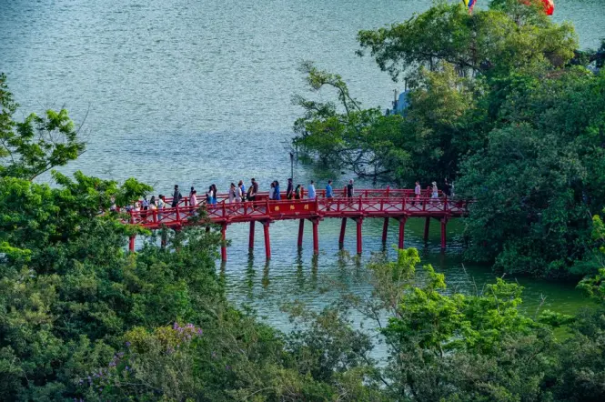 Visitors crossing the red Huc Bridge toward Ngoc Son Temple