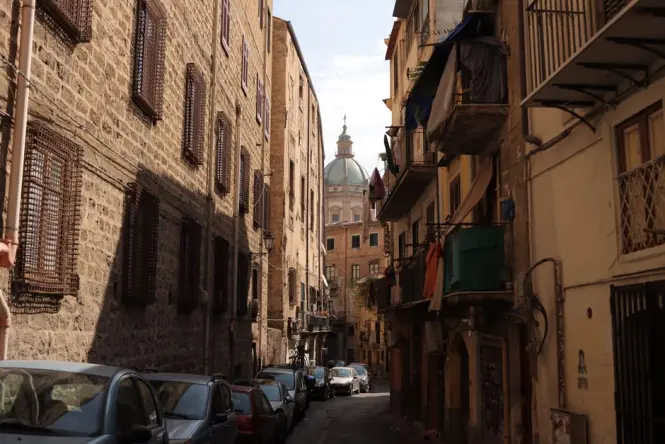 A sunny street leading toward the grand Porta Nuova arch near Palazzo dei Normanni
