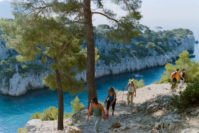 Hikers walking a limestone trail toward a calanque cove