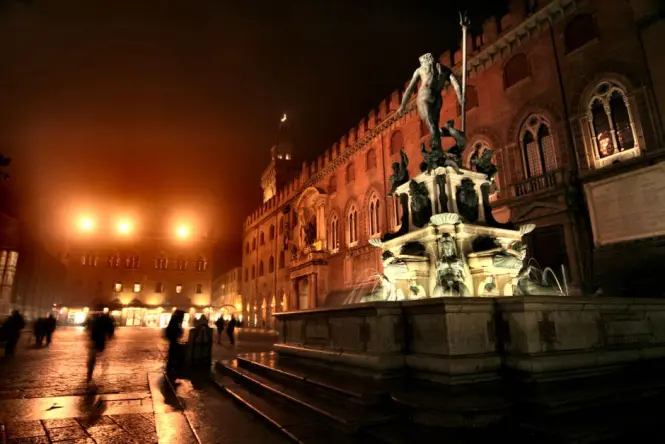 Piazza Maggiore in Bologna illuminated at night with people sitting on the steps