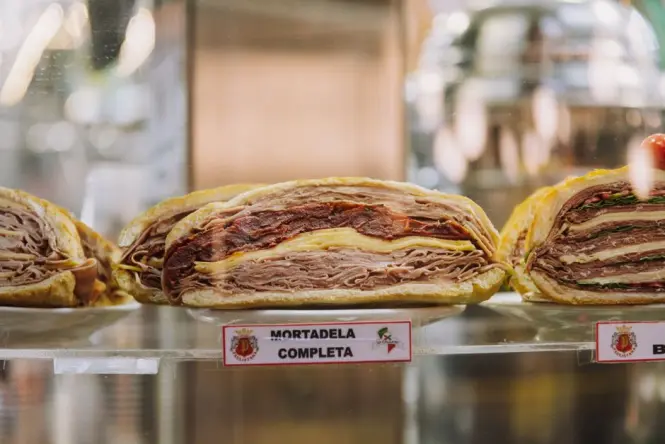 A wooden board of thinly sliced mortadella served with local bread