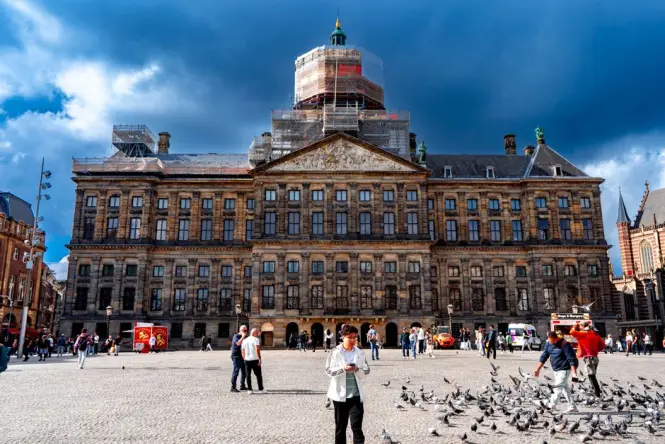 The grand stone facade of the Royal Palace Amsterdam on a clear day with Dam Square in the foreground